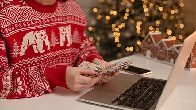 Woman counting ukrainian hryvnia bills, using laptop. Woman estimating money balance for shopping spree. Girl counting Christmas gifts.