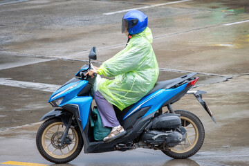 A motorcyclist wearing a raincoat rides on a wet street in rain, Bangkok, Thailand