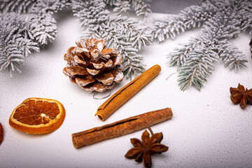 Obraz na płótnie Canvas Dried orange, anise and cinnamon among cones and snow-covered branches of a Christmas tree on a white snow-covered background