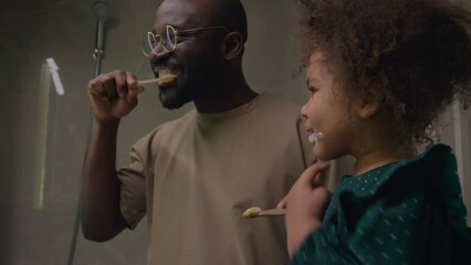 Father and daughter having fun time following important hygiene routine of brushing teeth before bed