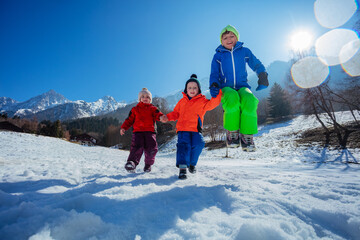 Kids laugh, jump in snow at sunny winter camp over mountains
