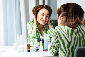 Happy woman in green long-sleeve poses at mirror touching hair