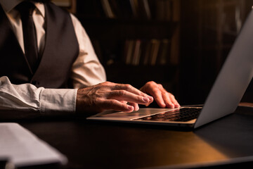 Concept of home office working. Close up businessman using laptop indoors. Business man wear formal waistcoat hands typing computer in dark room. Luxury expensive workplace