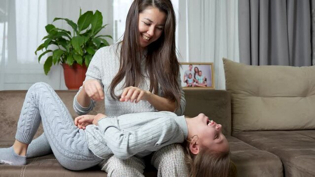 Daughter lies on mom knee on sofa at home.