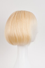 Naklejka premium Natural looking blonde fair wig on white mannequin head. Short hair cut on the plastic wig holder isolated on white background, side view.