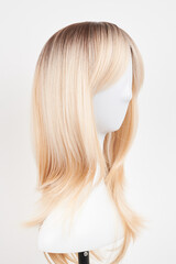 Natural looking blonde wig on white mannequin head. Long hair on the plastic wig holder isolated on white background.