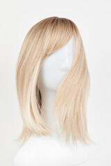 Naklejka premium Natural looking blonde fair wig on white mannequin head. Middle length hair cut on the plastic wig holder isolated on white background.