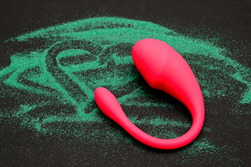Vibrator on a black background. Drawing on the sand in the form of a heart.