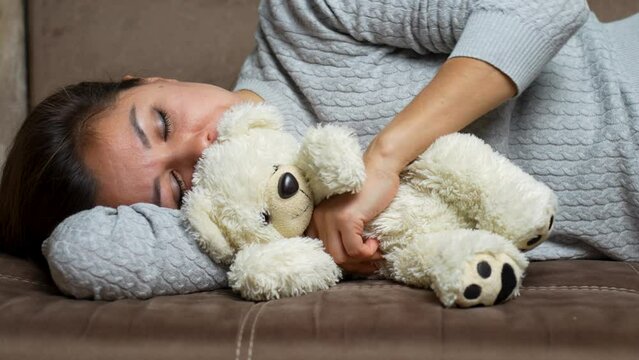 Sweet sleeping young woman with teddy bear on a couch, close-up