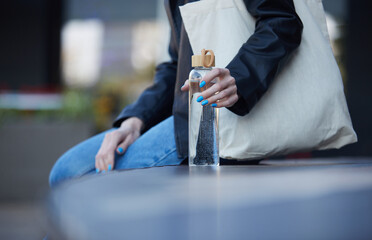 Female person sitting outdoors with a glass bottle of filtered water in hand.