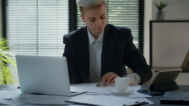 Female accountant rewriting data from paper diagrams into laptop spreadsheets app. Woman using computer when counting corporate costs. Confident blonde businesswoman doing paperwork in office