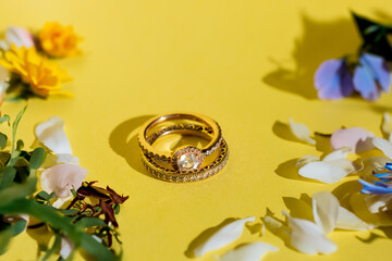 Engagement and wedding ring with diamonds over yellow background with flowers, petals and plants....
