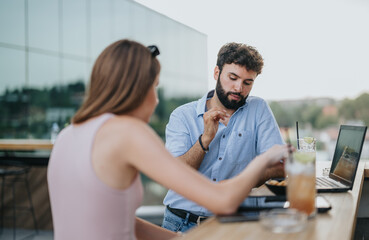 Young business partners discussing new projects in an urban cafe on a cloudy day. With efficient communication, they plan for business growth and market expansion.