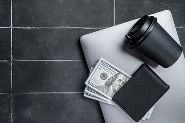 Top view of laptop, wallet with dollars and cup of espresso coffee. Black background. Top view. Copy space