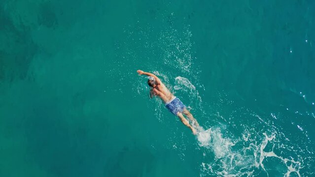 Aerial view of young man swimming in the sea. Man actively swimming in turquoise sea