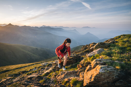 Female trail runner ascending alpine trail in the mountains at sunrise