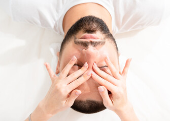 Male face massage for reducing puffiness by professional massage therapist in beauty clinic