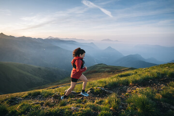 Naklejka na ściany i meble Female trail runner ascending alpine trail in the mountains at sunrise