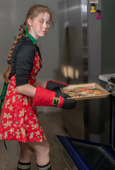 Girl Removing Christmas Cut-out Cookies from Oven, vertical