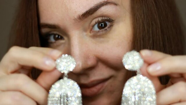 Closeup of a woman with wearing large jewelry earrings. Girl wearing luxury expensive jewelry with shining diamonds and precious stones. Female hands hold and showing earring.
