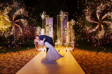The bride and groom on the wedding ceremony venue with fireworks at night . 