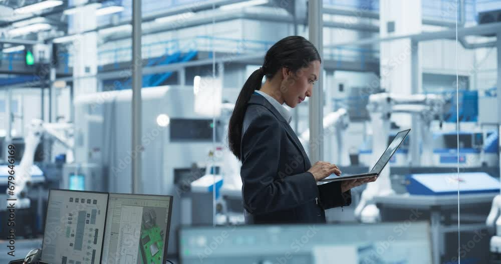 Poster Production Line Technician Working on a Laptop Computer at a Factory Office. Asian Female Software Specialist Updating Code for Machine Production and Assembly with Automated Robotic Arms