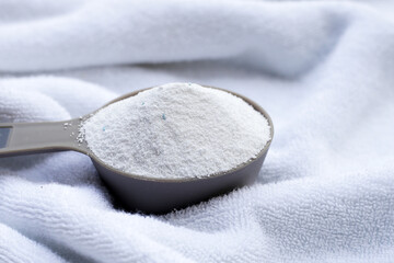 Detergent powder in measuring spoon with towel. Laundry concept.