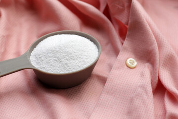 Detergent powder in measuring spoon on white before washing. Laundry concept.