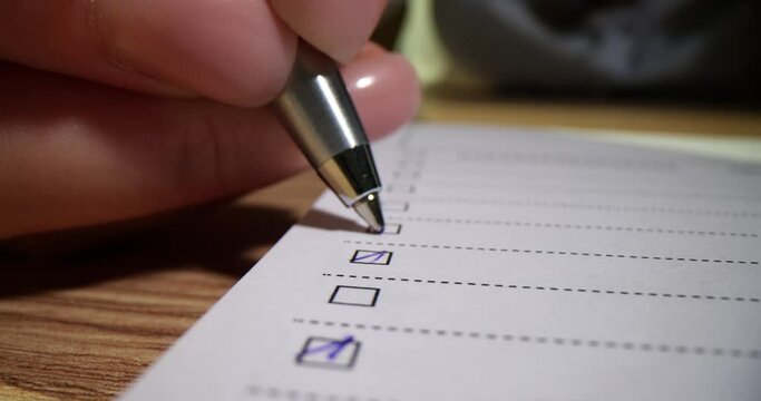 Closeup of hand checking or ticking blue pen on checklist checkbox and to-do list