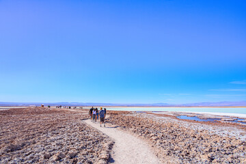 Turistas caminhando na Laguna Tebenquiche, um lago de sal com cores azul, verde e amarela ao lado do vulcão Licancabur. 