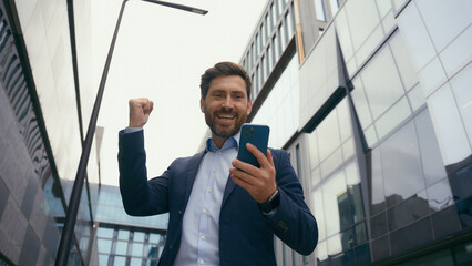 Caucasian middle-aged adult businessman in city business employer winner man guy entrepreneur manager with mobile phone win victory achievement cashback financial prize winning success in city happy - obrazy, fototapety, plakaty