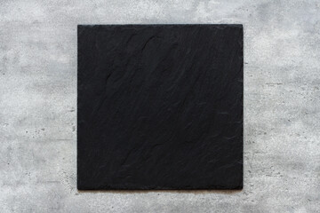 Black slate board on gray textured stone background, top view