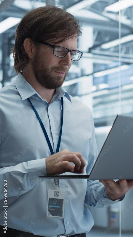 Poster Vertical Screen: Portrait of a Handsome Engineer with Glasses Using Laptop Computer and Looking Around a Factory Facility with Equipment Producing Modern Electronic Components for Different Industries