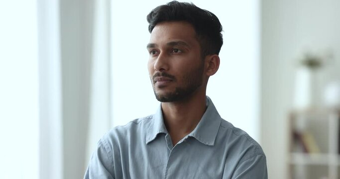 Serious thoughtful handsome young Indian man looking away, turning face to camera, getting happy, positive, smiling. Cheerful startup project leader, business professional in casual portrait