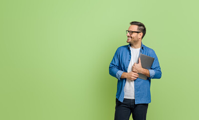 Smiling young businessman holding digital tablet and looking away thoughtfully on green background