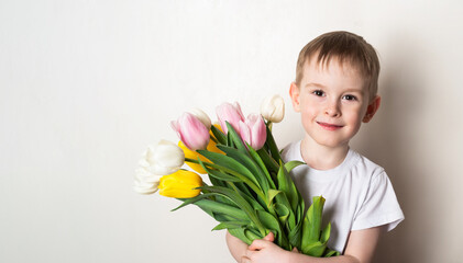 Banner. Portrait of a smiling boy with freckles in a white t-shirt with a bouquet of tulips on a white background.