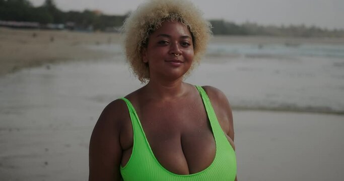 A young plus size African American woman walking along the beach and flirting. A beautiful African-American woman with large breasts in a swimsuit walks towards the camera.