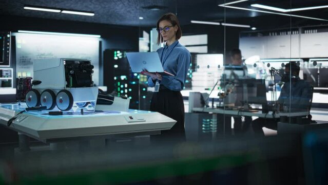 Portrait of a Female Programmer Using Laptop Computer to Write Code For a Remotely Controlled Robot. Elegant Woman Working in High-tech Lab, Gathering Data in a Advanced-Technology Project