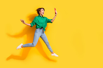 Fototapeta na wymiar Full length photo of shiny excited girl dressed green shirt jumping talking selfie modern device empty space isolated yellow color background