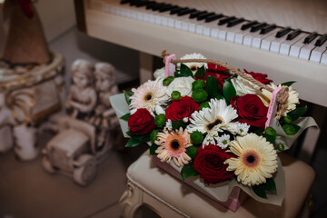a beautiful bouquet of flowers, a gift in a wooden box against the backdrop of a grand piano and an elegant antique interior. greeting card. roses, gerberas, green buds. desktop background.