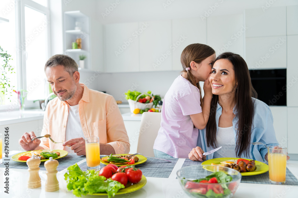 Poster Photo of cheerful tricky married couple small daughter eating dinner telling gossips indoors home kitchen