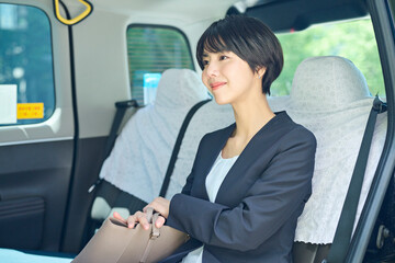 タクシーに乗る30代女性会社員 © One