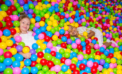 Fototapeta na wymiar Happy girl playing in ball pit on birthday party in kids amusement park and indoor play center. Child playing with colorful balls in playground ball pool.