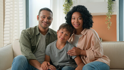 Multiracial African American Caucasian happy family portrait at home smiling parents father and mother hug little boy child preschool kid on sofa couch diverse generation parenthood love children care - obrazy, fototapety, plakaty