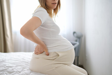 Future mother sits in bedroom feeling persistent ache in lower back. Lady gently rocks body...