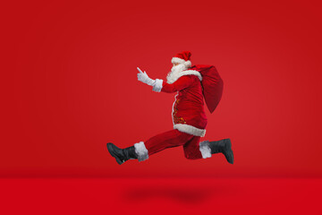 Fototapeta na wymiar Santa Claus jumps and runs forward fast, isolated on red background