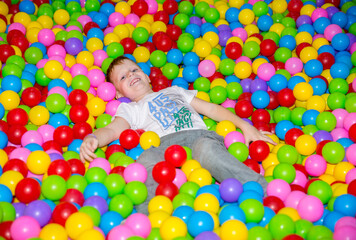Happy boy playing in ball pit on birthday party in kids amusement park and indoor play center. Child playing with colorful balls in playground ball pool.