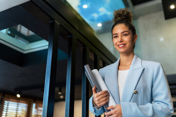 Successful businesswoman, she leaves her modern glass office, descending the staircase with important documents in hand.