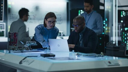 Diverse Group of Industrial Robotics Specialists Gathered Around a Table, Using Laptop Computer to Discuss Blueprints and Machine Components. Team Effort by Discussing Ideas to Optimise Product