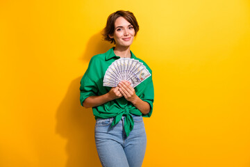 Photo of pretty adorable girl dressed green shirt holding cash fan smiling isolated yellow color...